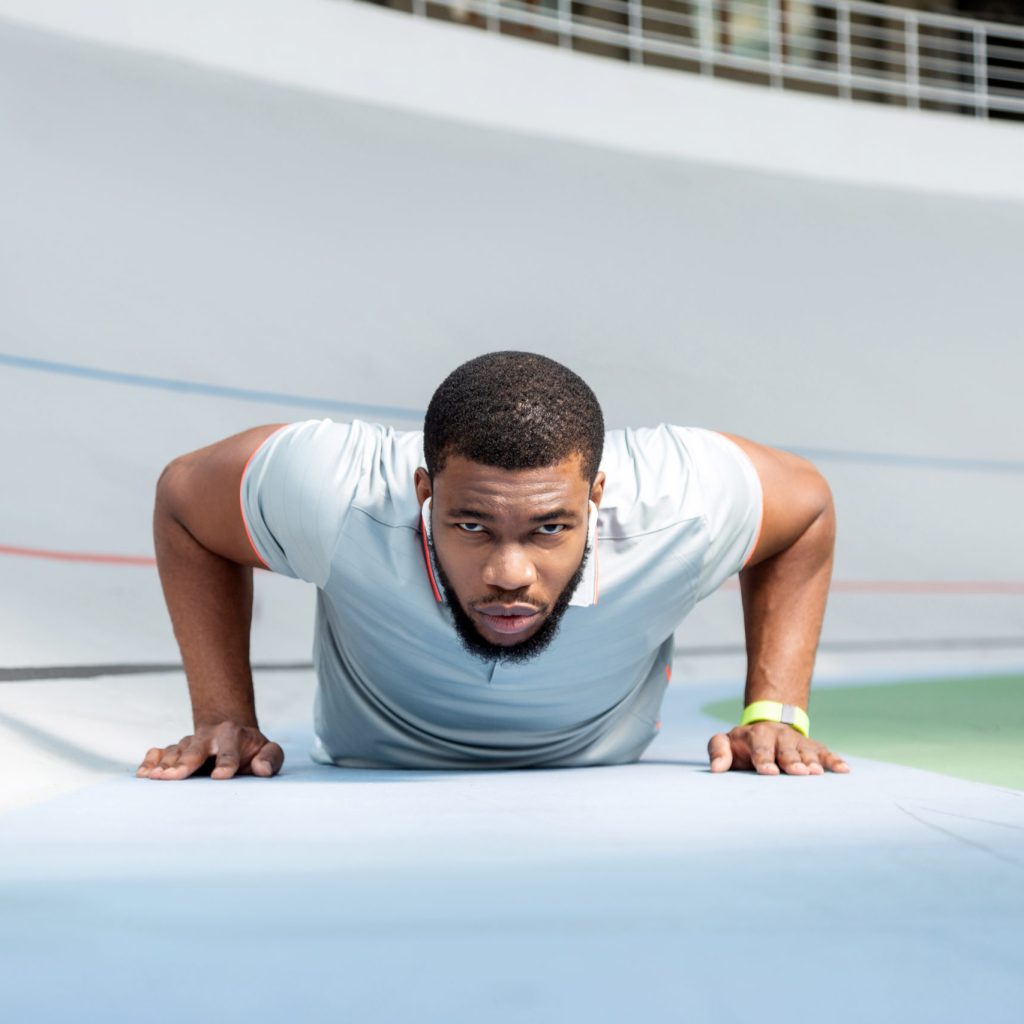 Determined athletic young man doing push-ups at the stadium while looking in front of him
